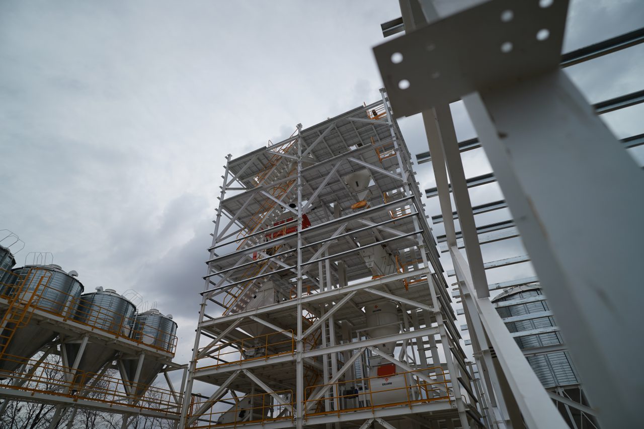 Exterior structure of a layer feed mill, with elevated hoppers and a bucket elevator tower