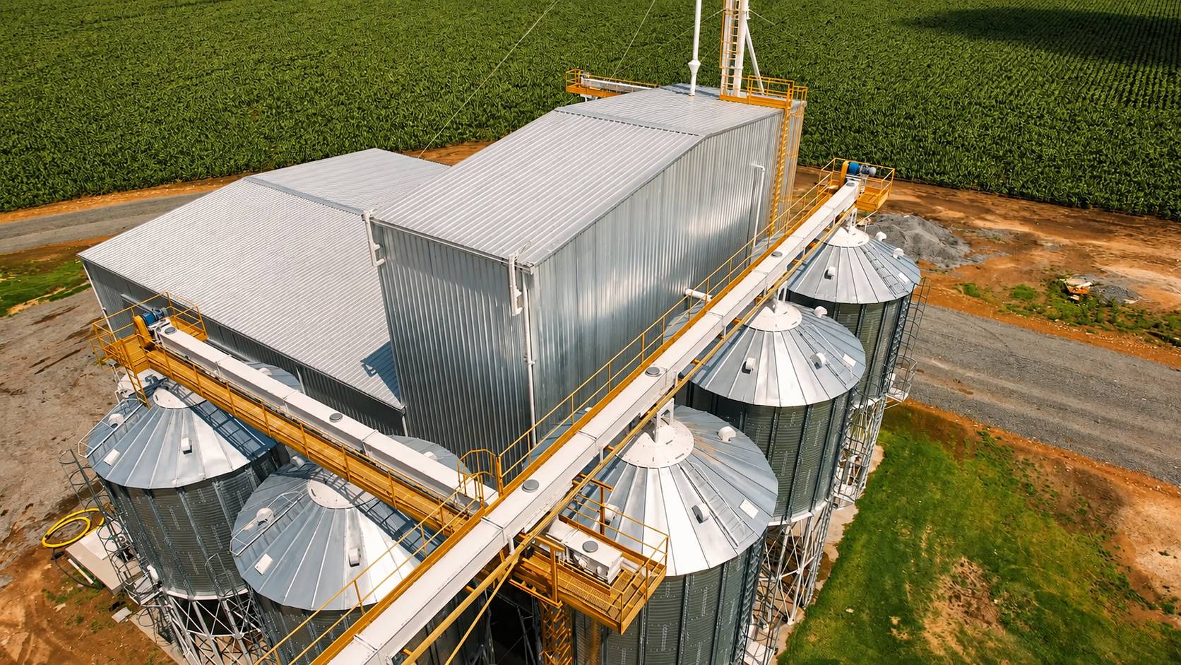 Aerial view of a compact feed mill at the edge of a sown field, with galvanised silos, walkways and process building