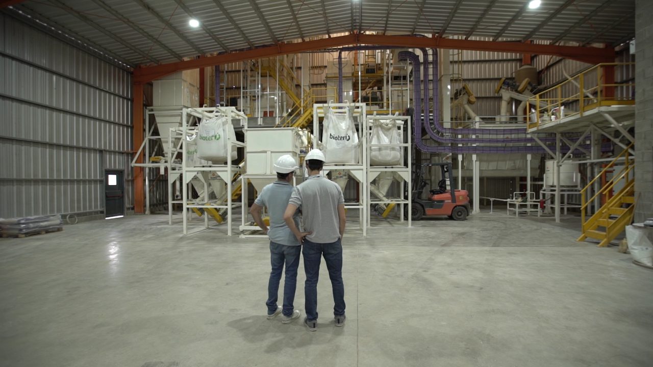 Dois operadores diante da linha de produção de ração para suínos, no interior da fábrica